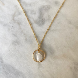 Gold necklace with a circular pendant featuring a white stone on a marble surface