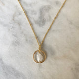 Gold necklace with a circular pendant featuring a white stone on a marble surface